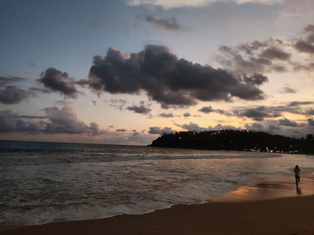       A person walking along a beach at sunset.
  