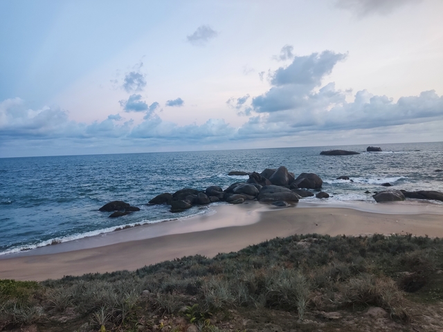       Beach with rocks and ocean waves under a cloudy sky.
  
