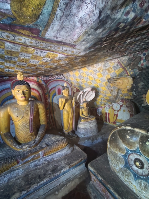       Interior view of a cave with Buddha statues and colorful murals.
  