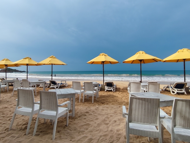 Beachside lounge chairs and tables with yellow umbrellas.