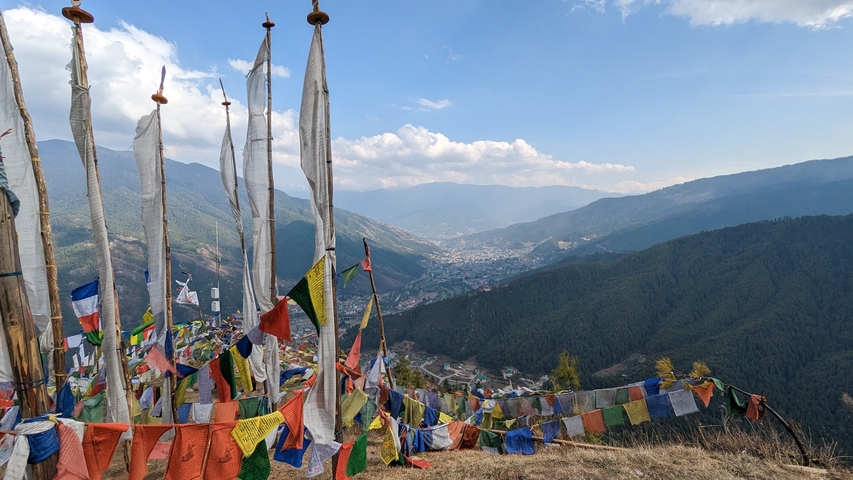       Colorful prayer flags atop a hill with a city view in the distance.
  