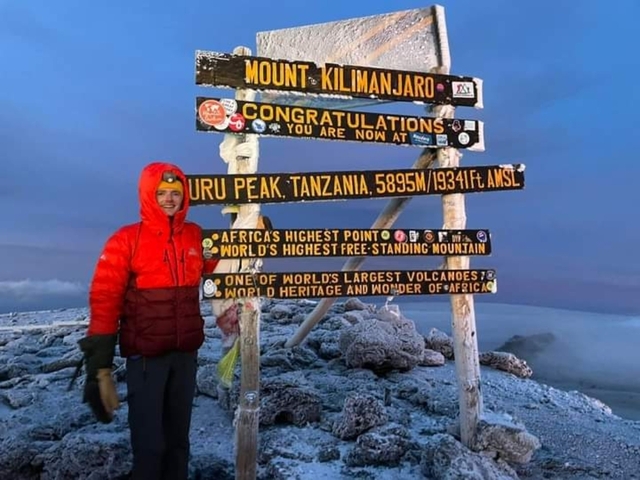 Person standing next to signs at the summit of Mount Kilimanjaro.