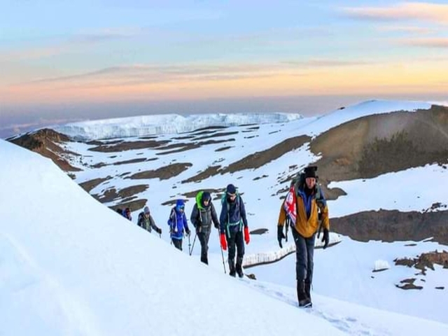 Hikers traversing a snowy landscape with mountains in the background.