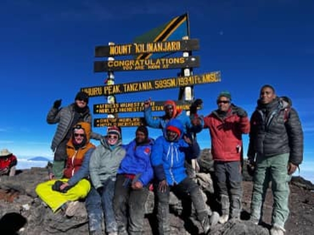 Group of climbers posing at the summit of Mount Kilimanjaro with signs.
