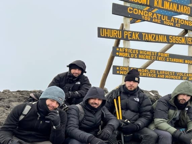Group of hikers posing at Uhuru Peak sign.