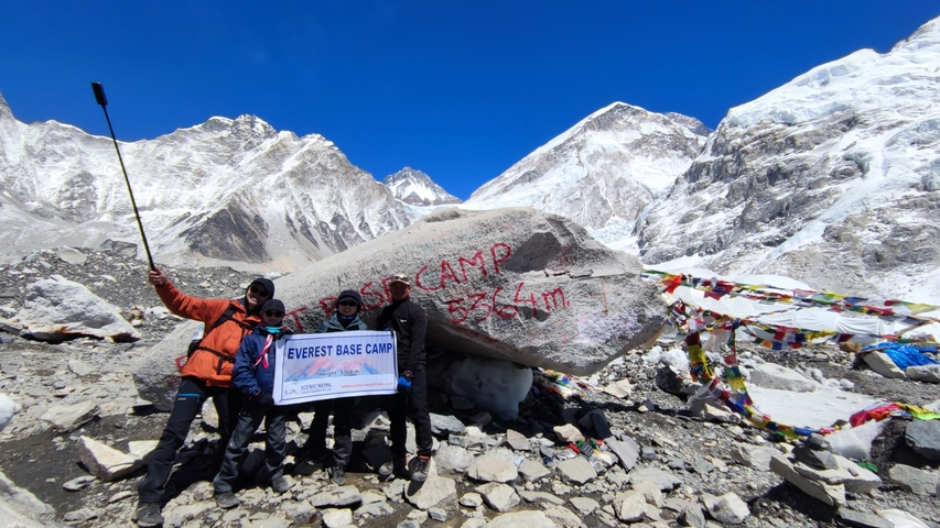 Group posing with Everest Base Camp marker with mountains in the background.
