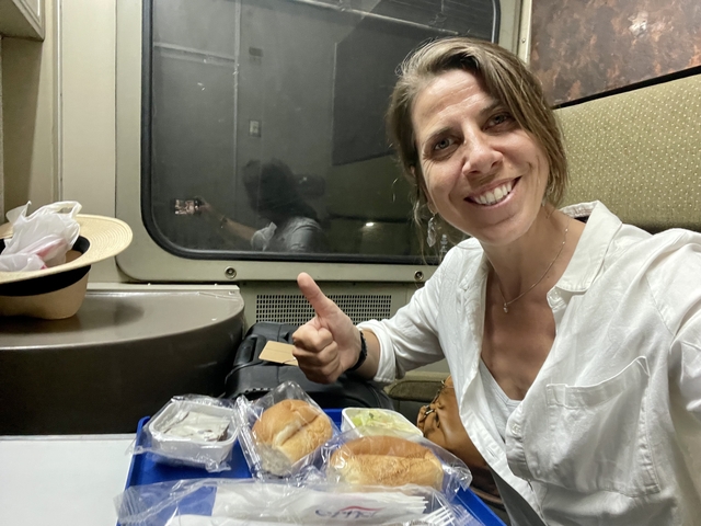 Smiling woman giving thumbs up with meal on a train.