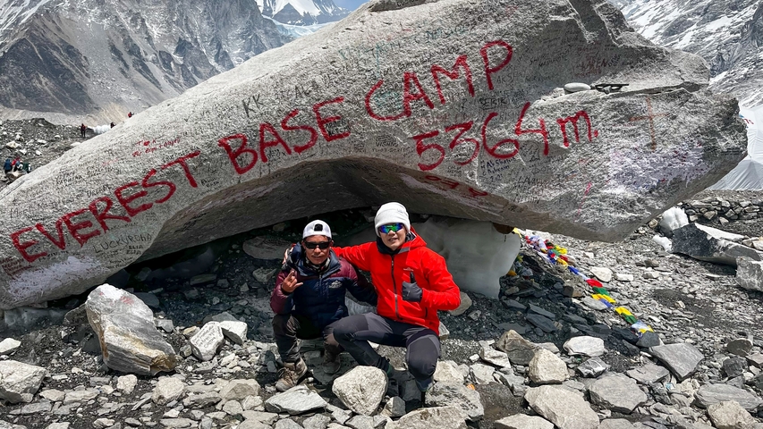 Two people posing in front of the Everest Base Camp rock.