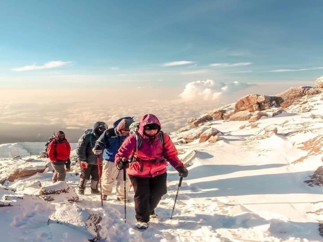 Hikers climbing snowy slopes with beautiful clouds.