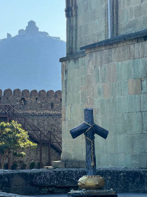       A stone cross with mountains in the background.
  