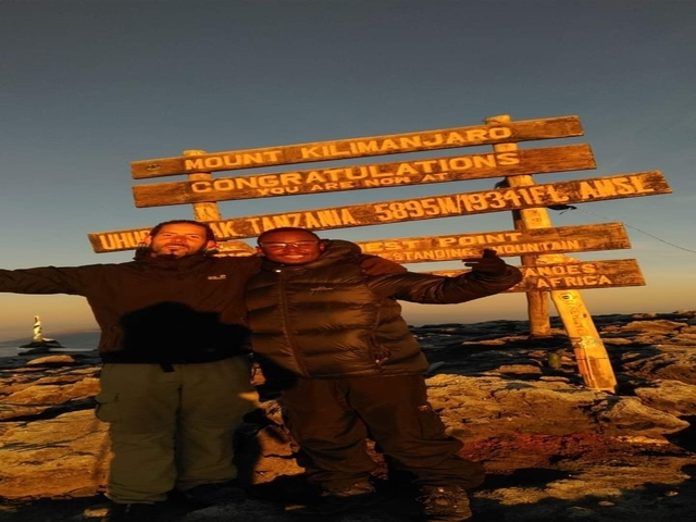       Two hikers standing at Uhuru Peak sign during sunset.
  