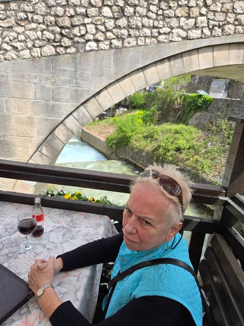       Person sitting at a cafe with a stone bridge and river in the background.
  