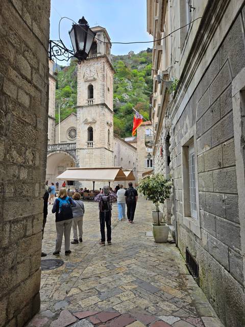       Narrow street with historical buildings and people walking.
  