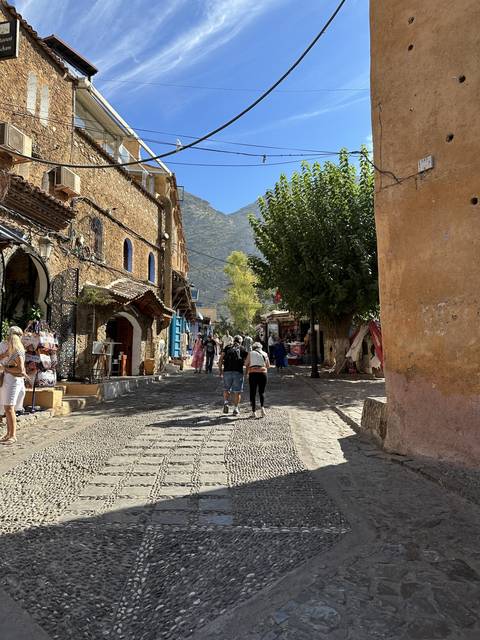 People walking in a scenic alley with mountains in the background.