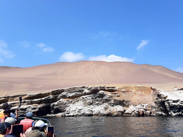       Candelabra geoglyphs on a sandy hill with people in a boat.
  