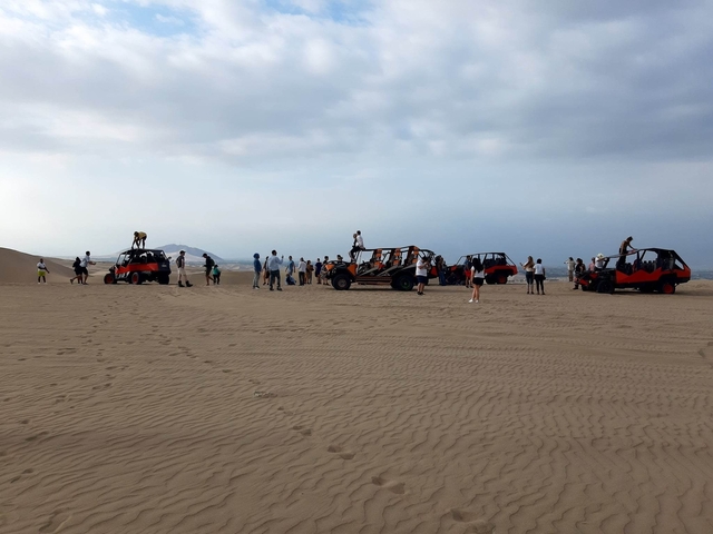       People with dune buggies on desert dunes.
  