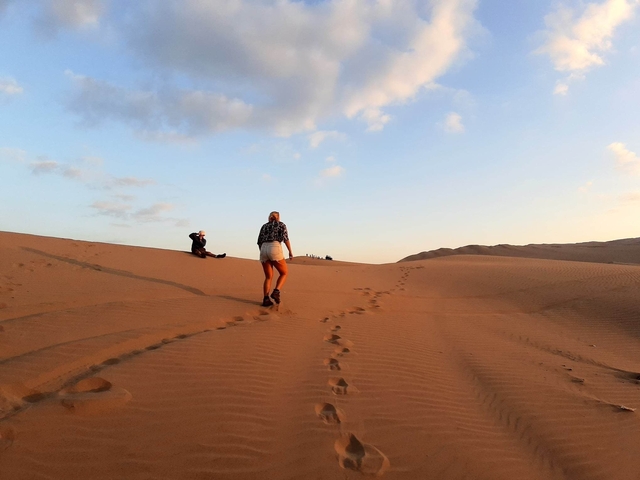       Person walking on a desert dune at sunset.
  
