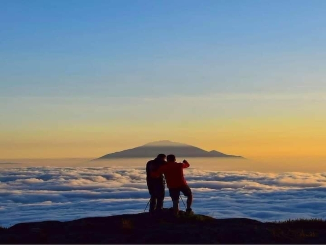 Two people photographing a sunrise over the clouds.