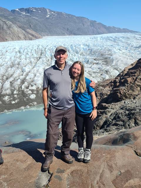       Two people posing in front of a large glacier.
  