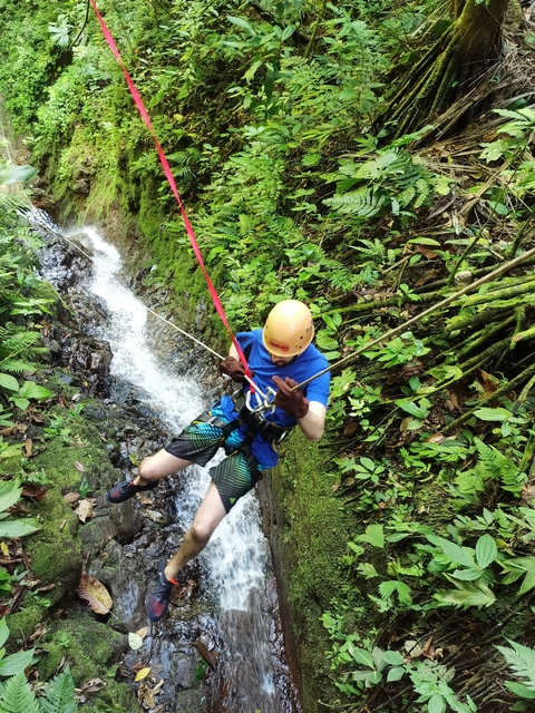 Person gripping ropes while descending near a waterfall.