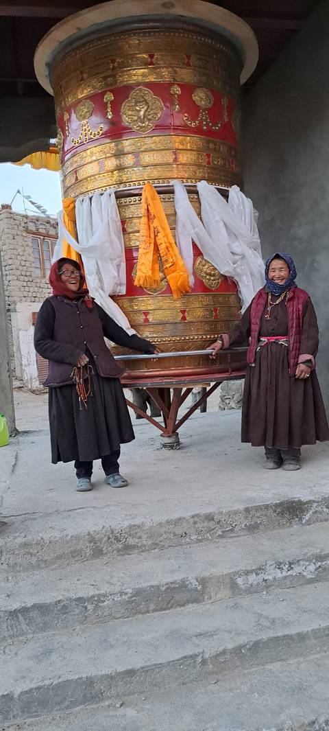 Two people standing beside a large prayer wheel.