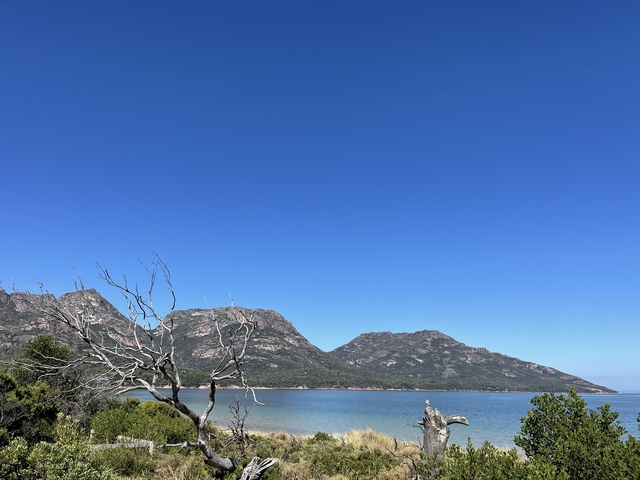       Mountain landscape by the water under a clear blue sky.
  