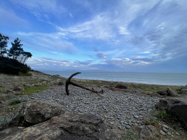       Rusty anchor by the seashore against a cloudy sky.
  