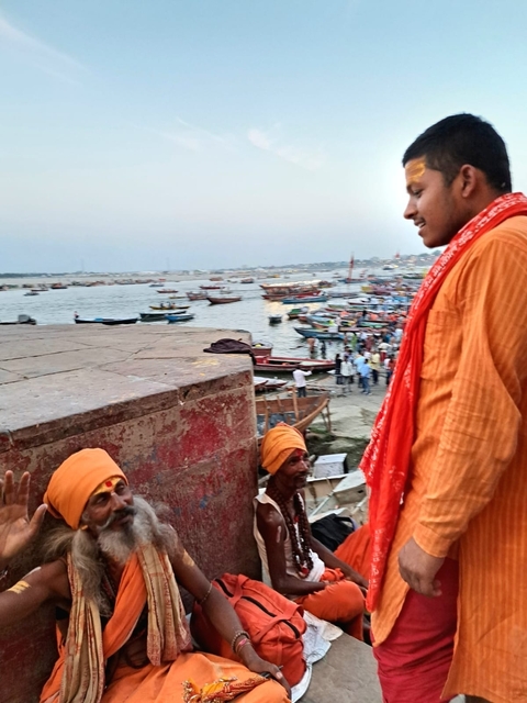 Colorful scene of people by the Ganges River with boats in the background.