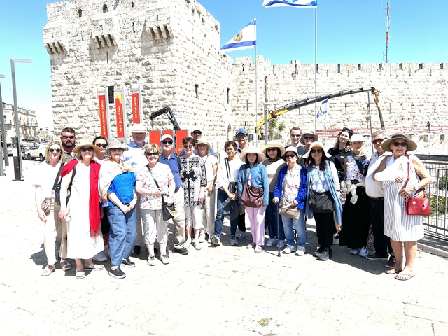       Group of tourists posing in front of an ancient wall.
  