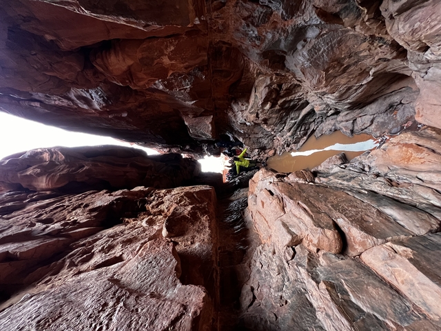       Narrow canyon with people walking and a small pool of water.
  