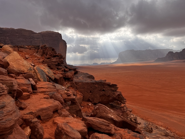       Dramatic desert landscape with red rocks and sunlight streaming through clouds.
  