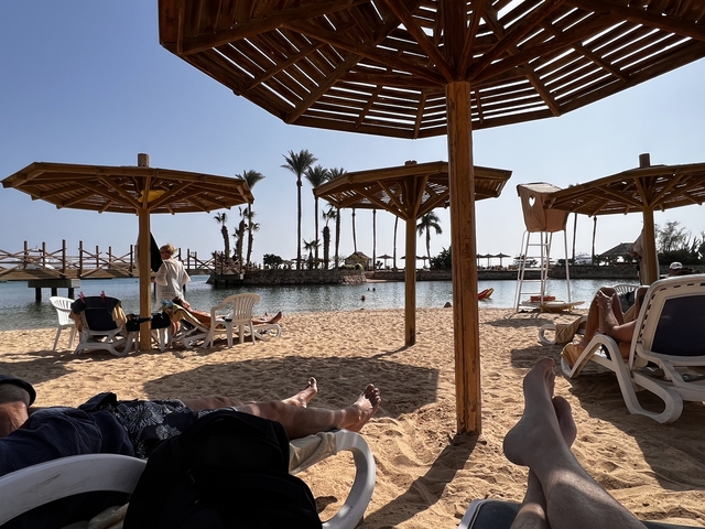       Beach scene with people relaxing under wooden umbrellas.
  