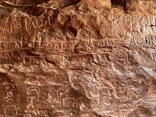       Carved ancient inscriptions on a red rock surface.
  
