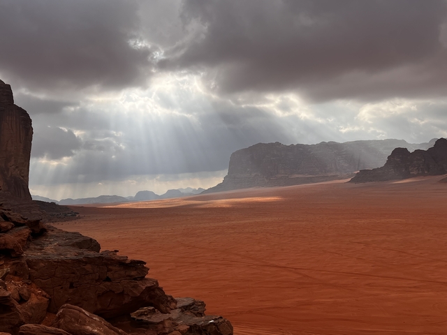       Dramatic desert landscape with sun rays breaking through clouds.
  