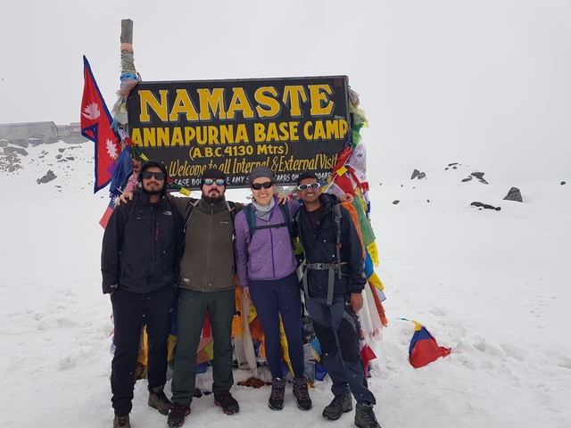       Group of hikers posing at Annapurna Base Camp with snow-covered surroundings.
  
