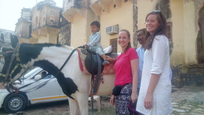       A child on a horse with surrounding people posing outside a building.
  