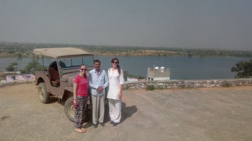       Three people standing by a jeep with a lake in the background.
  