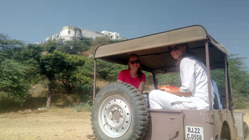       Two people sitting on a jeep with a building in the background.
  