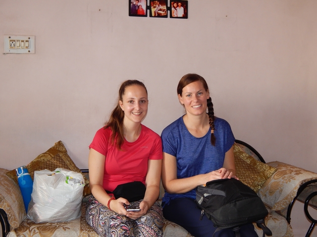 Two women sitting with bags on a couch indoors.