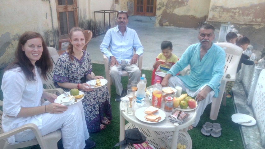       Group sitting around a table with food outdoors.
  
