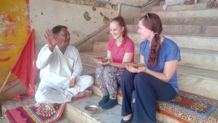       A man in white conversing with two women seated on stairs.
  
