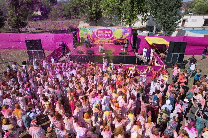       Group of people celebrating a colorful festival on a stage.
  