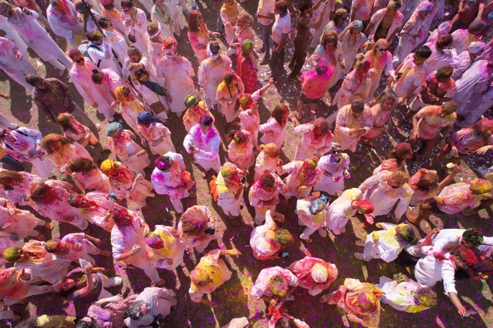       Aerial view of a crowd of people celebrating Holi covered in colorful powder.
  