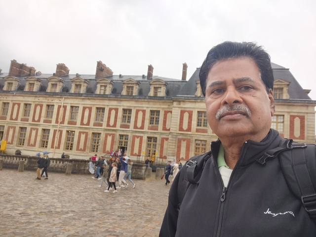 A man posing in front of a historic building with visitors.
