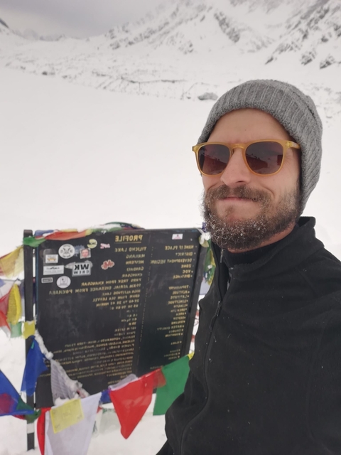       Person holding a sign with prayer flags in a snowy environment.
  
