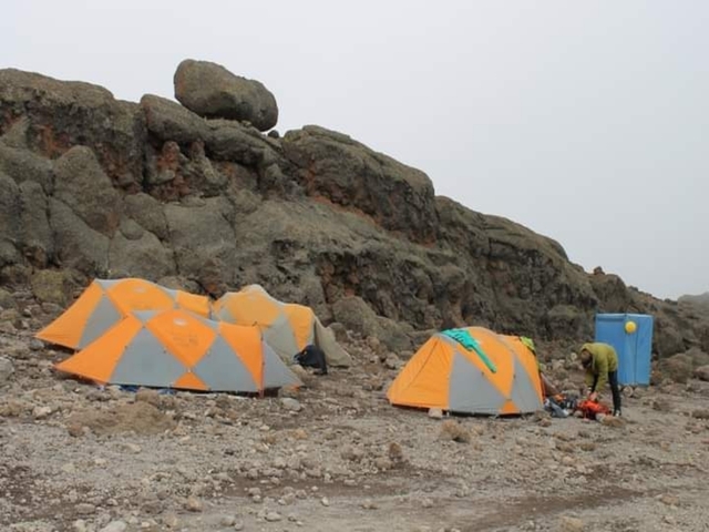       Camping tents on a rocky terrain with a person organizing gear.
  