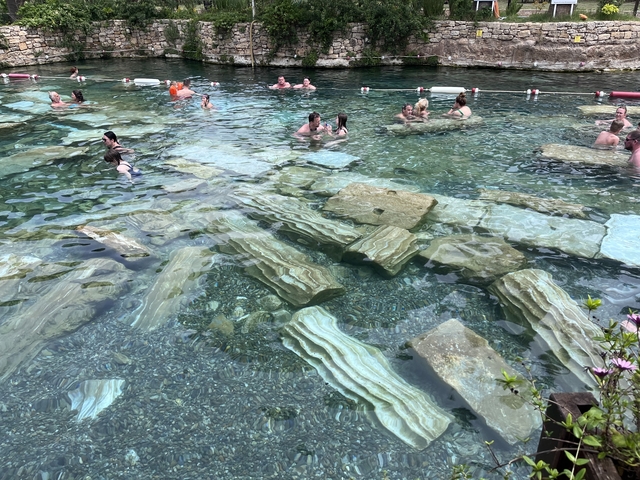People swimming in a pool with submerged ancient columns visible.