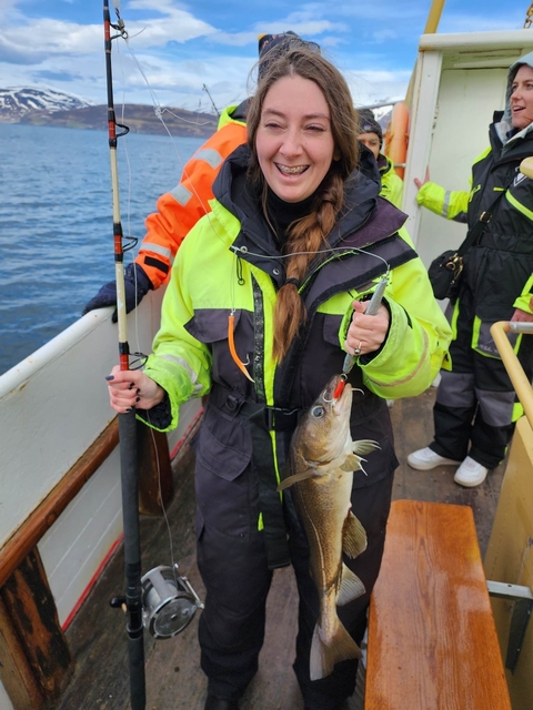 Person in a fishing outfit holding a fish on a boat.