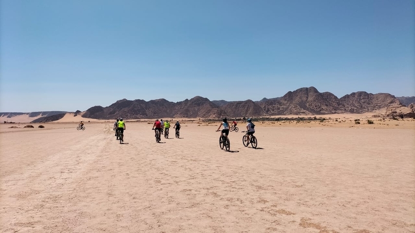 Group of cyclists riding through a desert with mountains in the background.