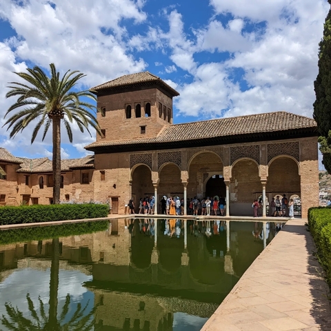       Crowd of tourists in an arched courtyard with water reflection.
  